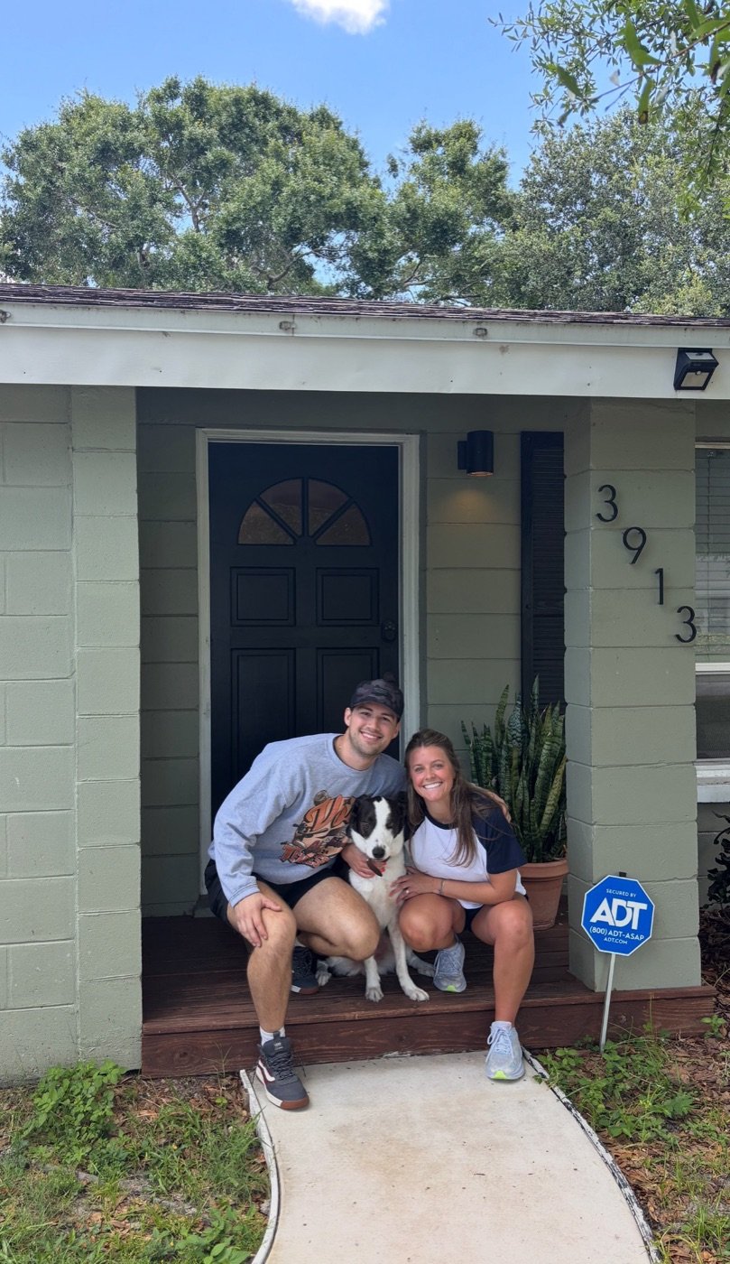 Two clients crouching with their dog on the front porch of their new home