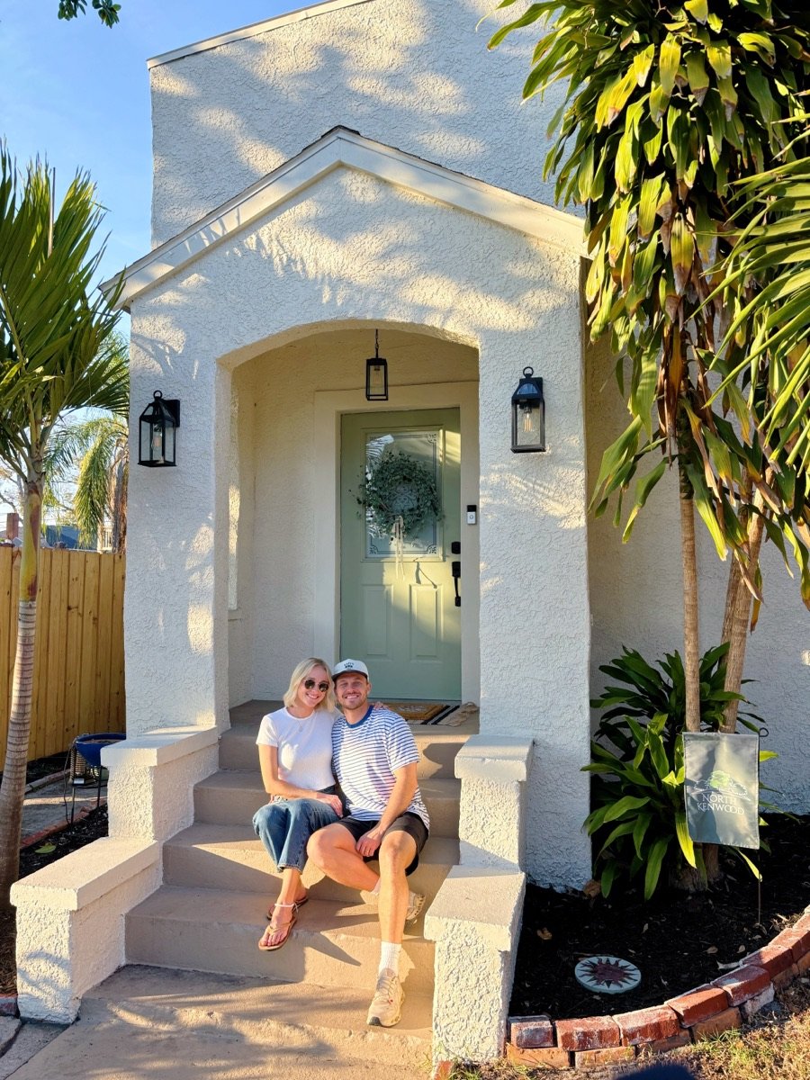 Rick and his wife sitting on the front steps of a white stucco bungalow