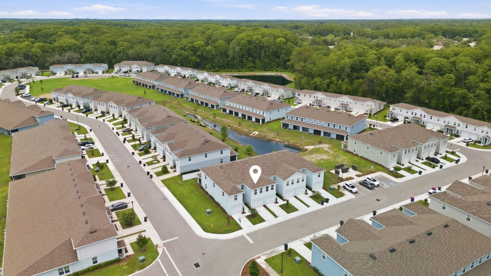 Aerial view of a townhome community with ponds and surrounding woods